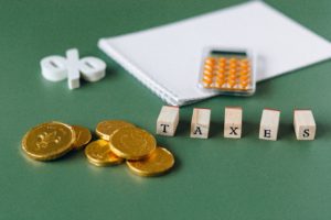 The word "taxes" spelled out in wooden blocks, with gold coins, a calculator, and percent sign on top of a green table.