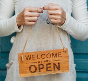 Person holding "Welcome we are open" sign. sign
