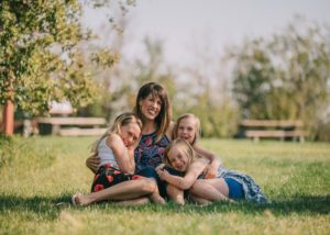 A woman hugging three girls in the grass outside.