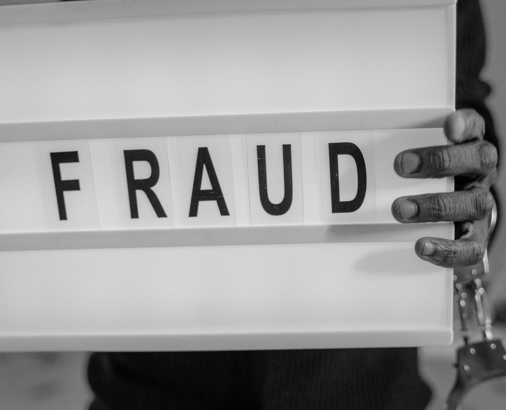 News Flash: Cloudgen LLC Pleads Guilty to H-1B Fraud Man holding sign that says fraud and wearing handcuffs.