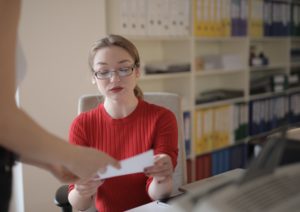 Woman in red sweater and glasses inspecting a piece of paper.
