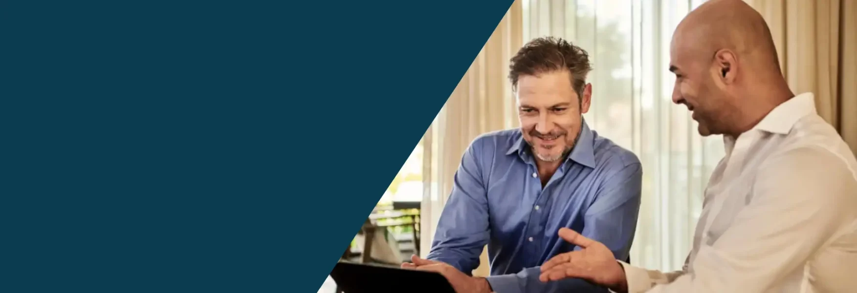 This is a banner image with half its left section colored in dark teal color and the other half there is an image of two business men working at a desk looking at a computer and some documents. In the background you see a window looking at the outdoors with greenery. The image signifies the freedom American businesses provide for investors along with the Shihab Burke LLC Immigration Lawyers brand.