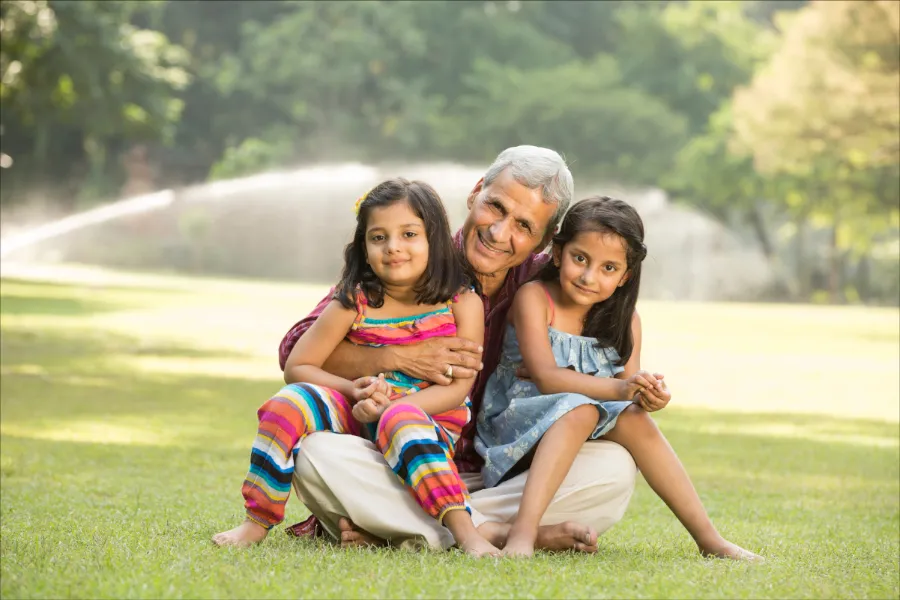 Image of grandparent with his granddaughters in a golf course. The grandfather is hugging his granddaughters and they are sitting down in a green field. The image represents the immigration lawyers at Shihab Burke LLC