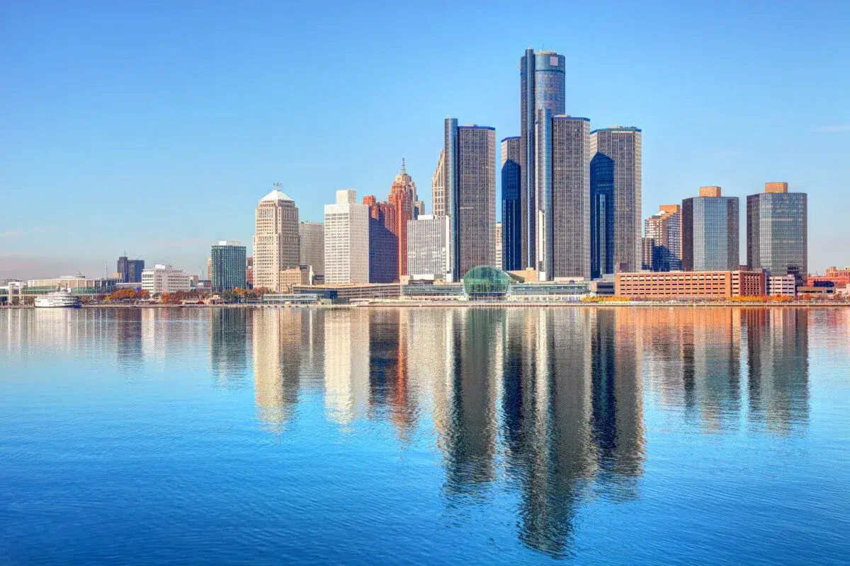 Image of cityscape in Troy Michigan. The picture is taken from across a lake and you can see multiple buildings rising up in the Troy, Michigan sky. The image represents the immigration lawyers of Troy Michigan.