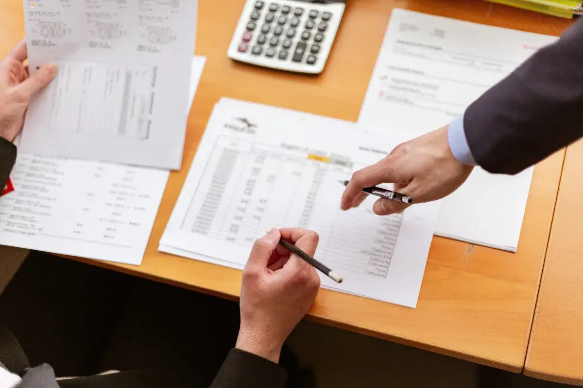 Picture of people working with papers on a desk. The image signifies the paperwork involved with Mergers and Acquisitions of companies.