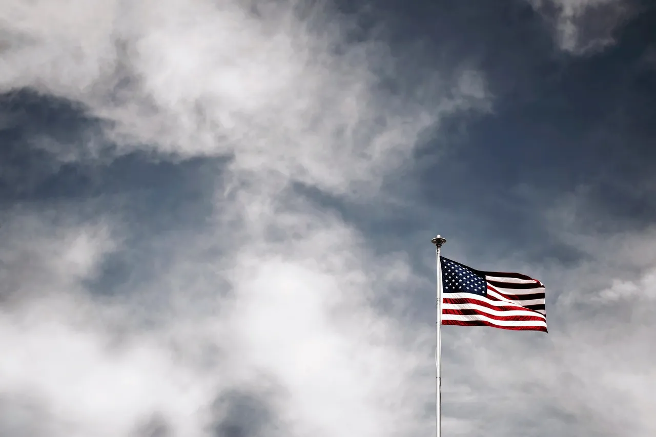 Image of an American Flag waving in a partially clouded sky. The image represents the U.S. Birthright citizenship