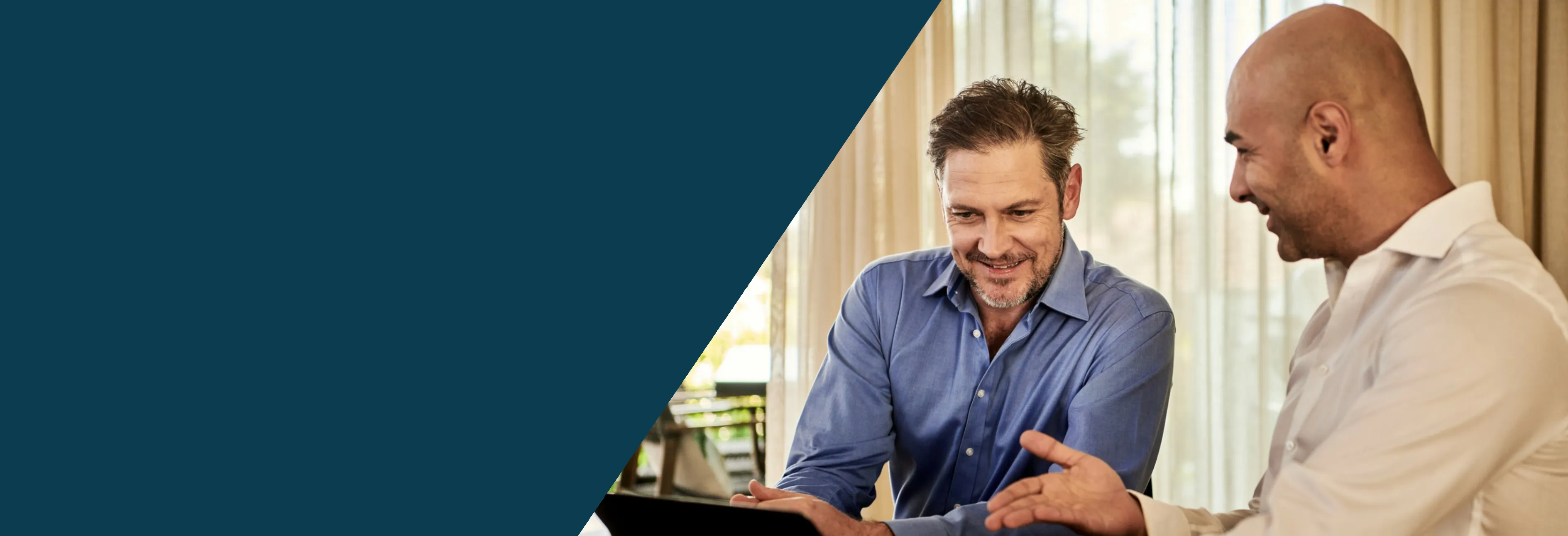 This is a banner image with half its left section colored in dark teal color and the other half there is an image of two business men working at a desk looking at a computer and some documents. In the background you see a window looking at the outdoors with greenery. The image signifies the freedom American businesses provide for investors along with the Shihab Burke LLC Immigration Lawyers brand.