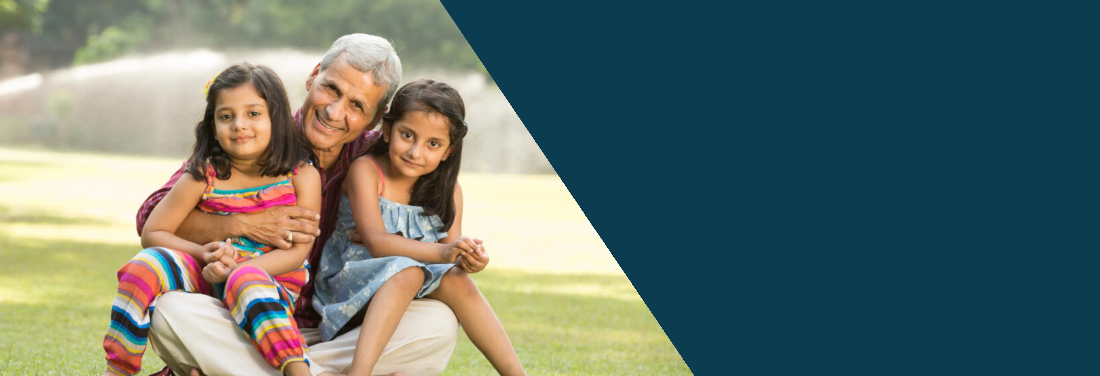 Banner Image for the website. To the left of the image is a grandparent embracing his both granddaughters in his arms sitting at a golf course. You can see the field of green behind them. They are sitting on the ground.